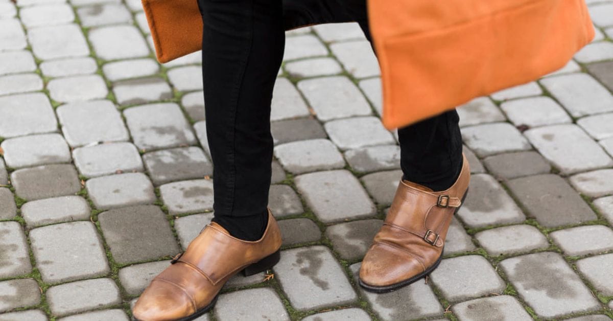 A person in brown shoes and an orange coat stands confidently, showcasing a stylish and vibrant outfit combination.